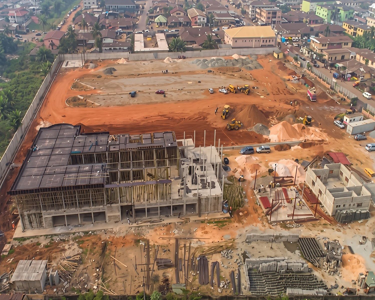 Aerial view of a construction site with a multi-storey building frame, excavators and stockpiled materials